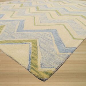 Plush rug featuring a large zigzag pattern in ivory, pale blue, and lime green on light wood planks.