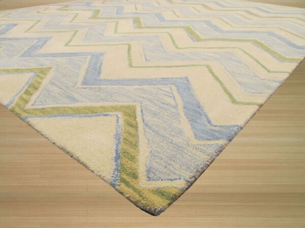 Plush rug featuring a large zigzag pattern in ivory, pale blue, and lime green on light wood planks.