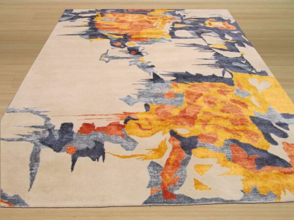 Beige rug featuring an abstract painterly pattern of golden yellow, rust, and slate grey on wood plank flooring.