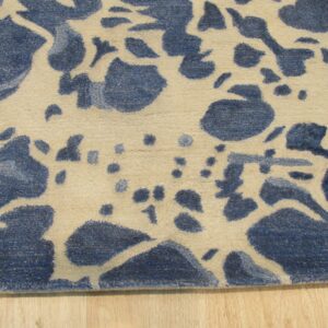 Medium pile rug in blue and beige with scattered abstract shapes on a natural wood floor.