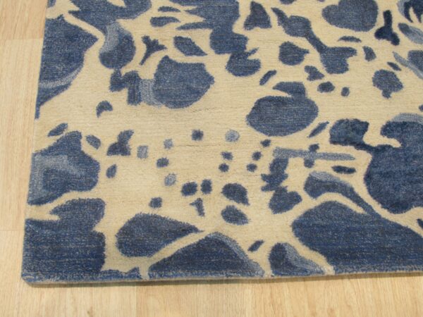 Medium pile rug in blue and beige with scattered abstract shapes on a natural wood floor.