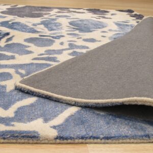 A blue and cream abstract patterned rug is partially rolled up, showing its gray backing on wood flooring.