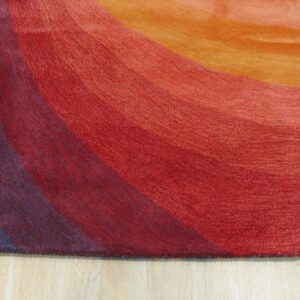 A textured rug displaying wide, curved color bands of blue, red, and orange on light wood flooring.