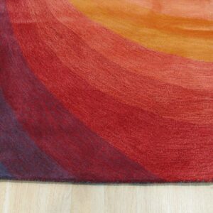 Textured low-pile rug displaying wavy color gradients in blue, red, and orange on light wood planks.