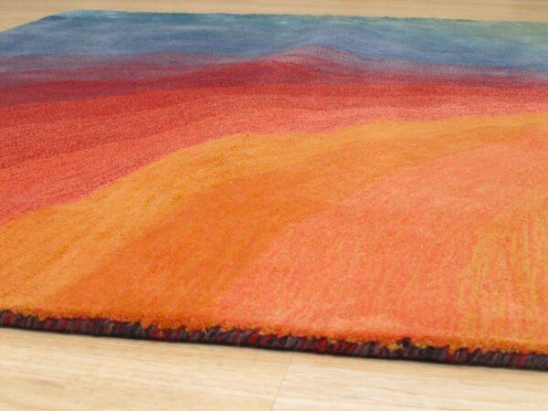Textured rug with thick orange, red, and blue wavy color bands on light wood flooring.