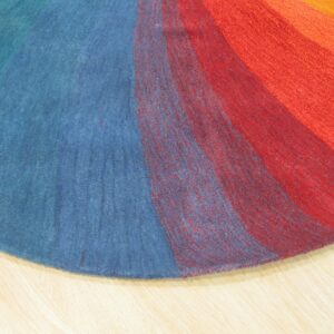 Circular rug section showing multicolored radial bands of blue, red, and orange pile on light wood.