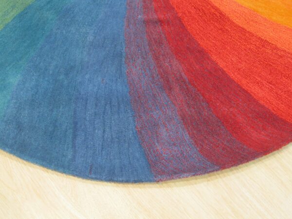 Circular rug section showing multicolored radial bands of blue, red, and orange pile on light wood.