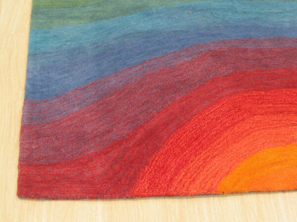 Abstract rug corner showing curved bands of green, blue, red, and orange on light wood flooring.
