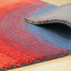 Colorful abstract rug in red, orange, and blue is folded over, revealing the gray backing on wood flooring.