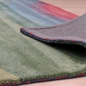 A low-pile abstract rug in green, blue, and red is curled back, revealing the gray backing on wood floor.