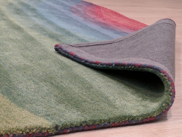 A low-pile abstract rug in green, blue, and red is curled back, revealing the gray backing on wood floor.