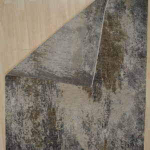 Abstract rug featuring distressed gray, beige, and brown colors, folded over on a light wood plank floor.