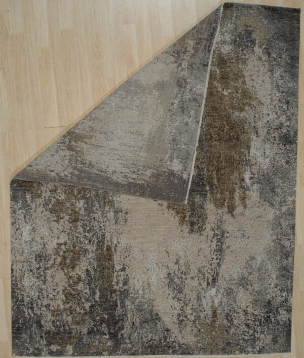 Abstract rug featuring distressed gray, beige, and brown colors, folded over on a light wood plank floor.