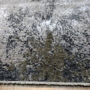 Abstract gray, black, and olive rug with a speckled pattern rests on light plank wood flooring.