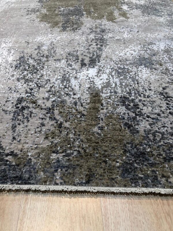 Abstract gray, black, and olive rug with a speckled pattern rests on light plank wood flooring.
