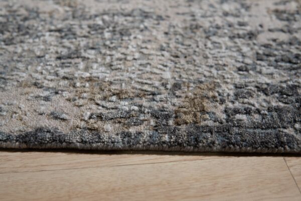 Close-up of a textured gray and beige abstract rug edge resting on wood flooring.
