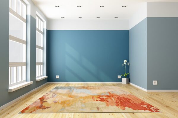 Abstract rug featuring orange, red, and blue tones on light wood flooring in a brightly lit room.