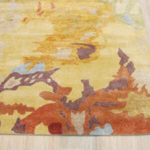 Close-up of a high-pile rug with abstract yellow, orange, maroon, and light blue shapes on pale wood flooring.