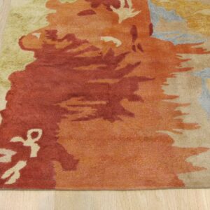 Abstract rust, orange, beige, and green rug detail shown on light wood plank flooring.