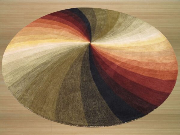 Round rug with a radiating, multi-color swirl pattern in warm earthy tones on light wood flooring.