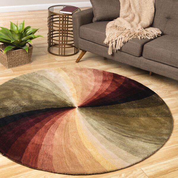 A round rug with radiating stripes of red, olive, and gold sits on wood flooring beside a brown sofa.