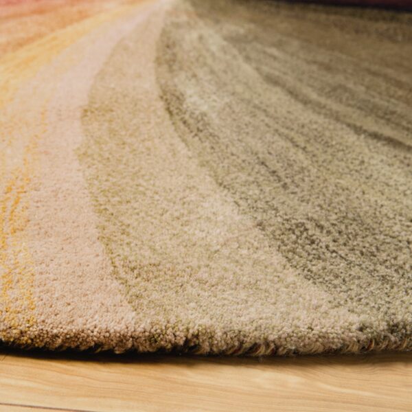 Detail of a plush rug showing curved bands of orange, gold, and olive green on light wood.