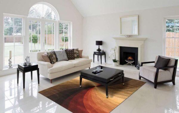 Radial patterned rug in shades of red, orange, and brown beneath a black table on white tile.