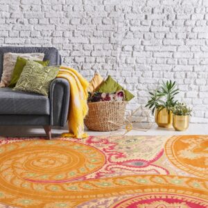 Low-pile orange rug with pink and green paisley patterns beneath a gray sofa and white brick wall.