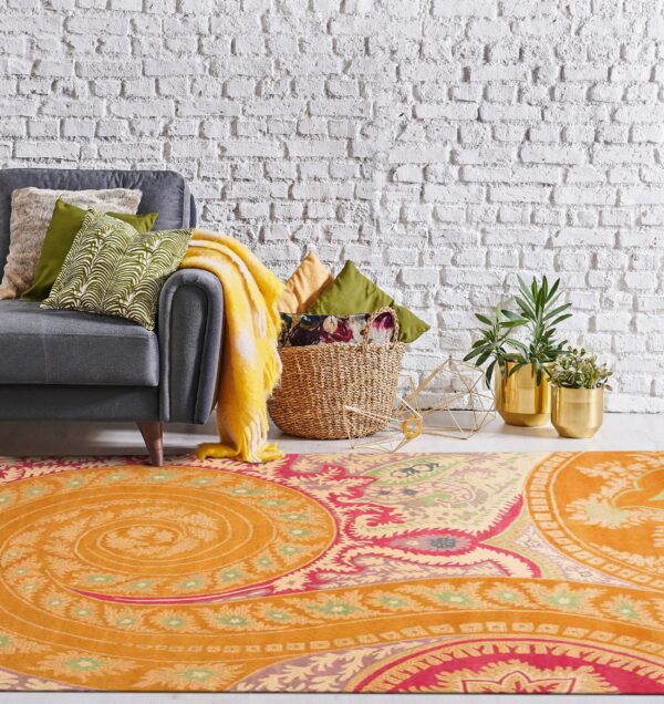 Low-pile orange rug with pink and green paisley patterns beneath a gray sofa and white brick wall.