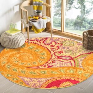 A round, colorful orange and pink paisley rug sits by a sunlit window and wooden chair.