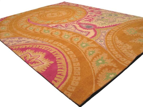 An amber rug featuring a large swirling medallion pattern in bright pink, pale green, purple, and cream colors.