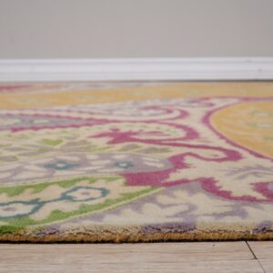 Low-angle view of a yellow, magenta, green, and cream patterned rug with medium pile on wood-look flooring.