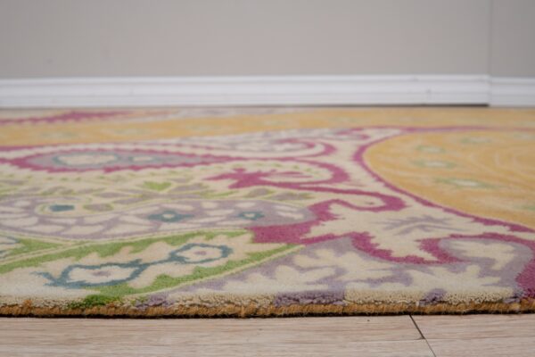 Low-angle view of a yellow, magenta, green, and cream patterned rug with medium pile on wood-look flooring.