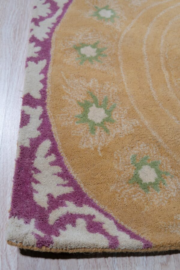 Tan, high-pile rug with a magenta and cream leaf border and green floral accents sits on light wood flooring.