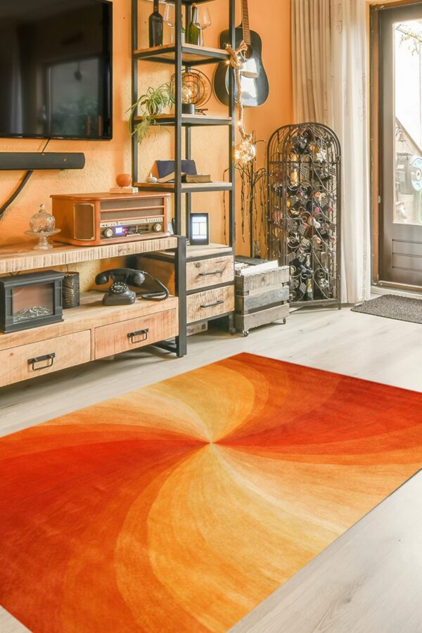 The orange and red vortex rug sits on light wood flooring in a rustic living room setting.