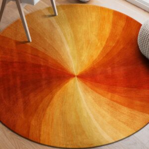 Round rug with orange and yellow gradient pattern on wood floor beside a chair leg and knit pouf.