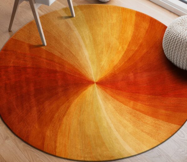 Round rug with orange and yellow gradient pattern on wood floor beside a chair leg and knit pouf.