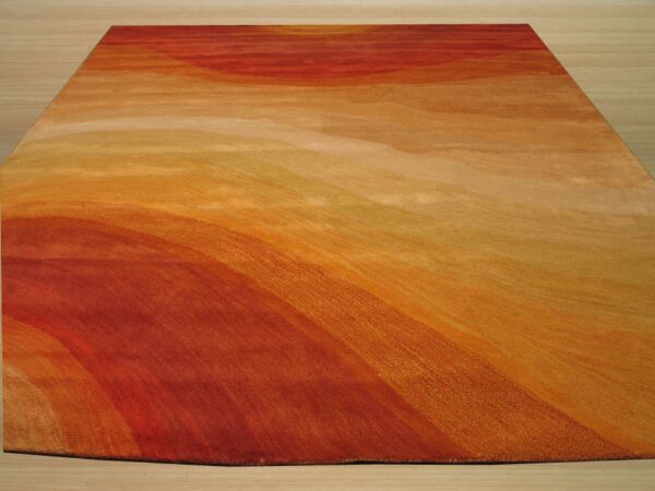 Abstract rug displaying a wavy gradient of red, orange, and gold colors on light wooden flooring.