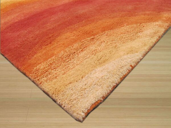 Shaggy rug corner displaying a high-pile red, orange, and cream color gradient on light wood flooring.