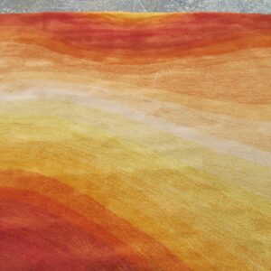 Abstract gradient rug in warm red, orange, and yellow tones resting on a speckled gray floor.