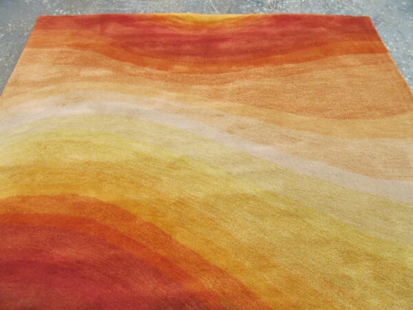 Abstract gradient rug in warm red, orange, and yellow tones resting on a speckled gray floor.