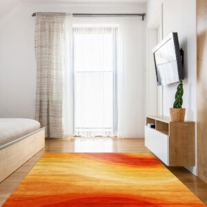 A large, abstract rug with red, orange, and yellow gradients lies on hardwood floor in a bright room.