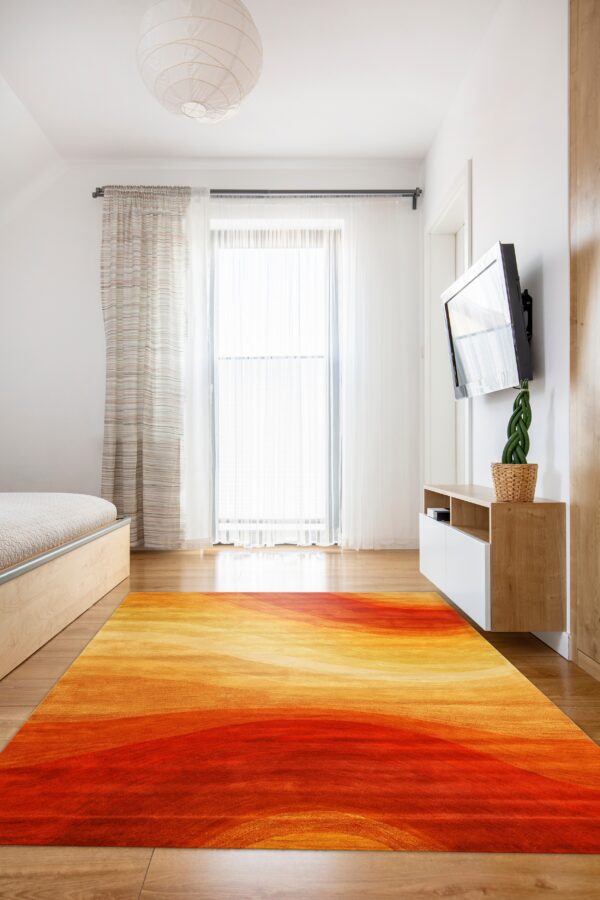 A large, abstract rug with red, orange, and yellow gradients lies on hardwood floor in a bright room.