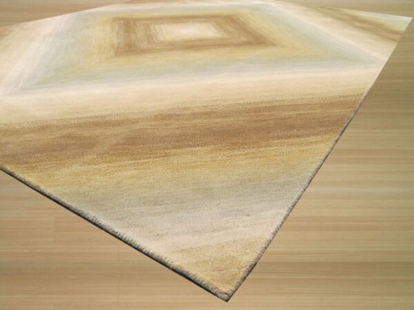 Tan and brown shaded rug with concentric square patterns sits on light wood plank flooring.