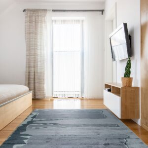 Highly textured gray and blue abstract rug anchors a modern bedroom with wood floors and white walls.
