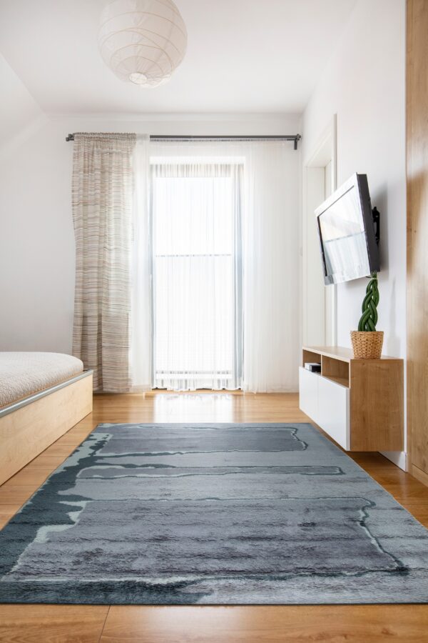 Highly textured gray and blue abstract rug anchors a modern bedroom with wood floors and white walls.