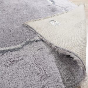 High pile grey shaggy rug flipped to reveal the tightly woven cream backing on light wood flooring.