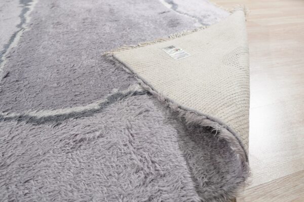 High pile grey shaggy rug flipped to reveal the tightly woven cream backing on light wood flooring.