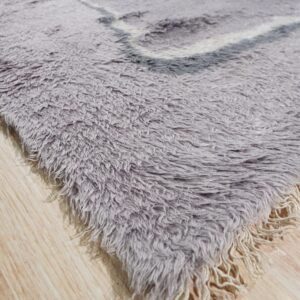 High pile gray shaggy rug featuring white geometric lines and light fringes on wood plank flooring.