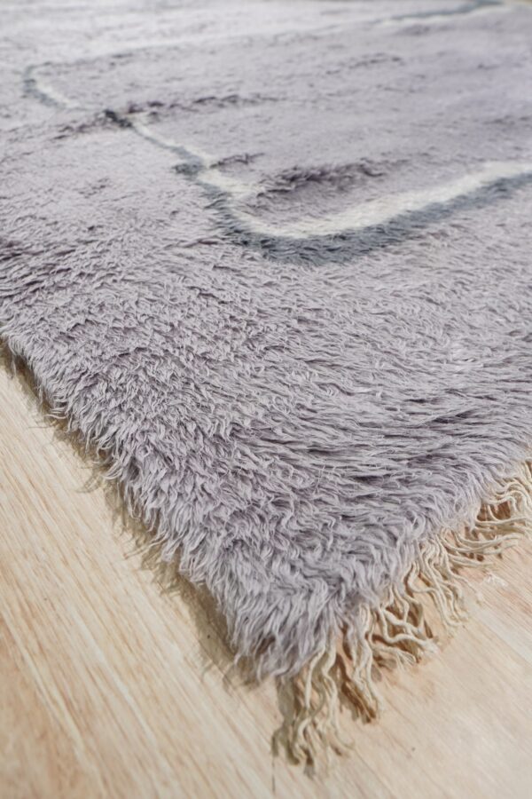 High pile gray shaggy rug featuring white geometric lines and light fringes on wood plank flooring.